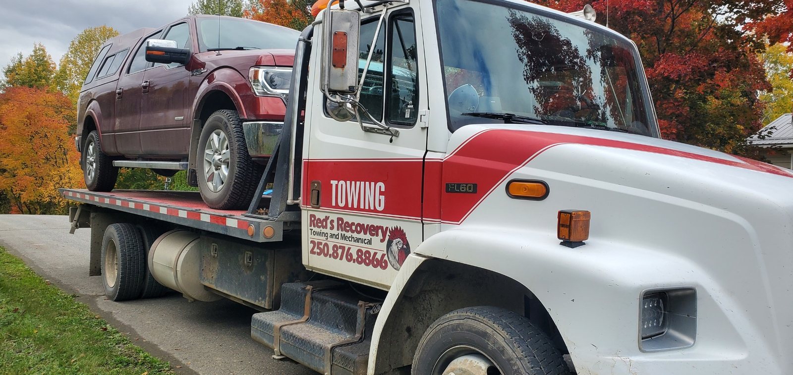 Ford pickup truck loaded on Red's Recovery flatbed tow truck in autumn